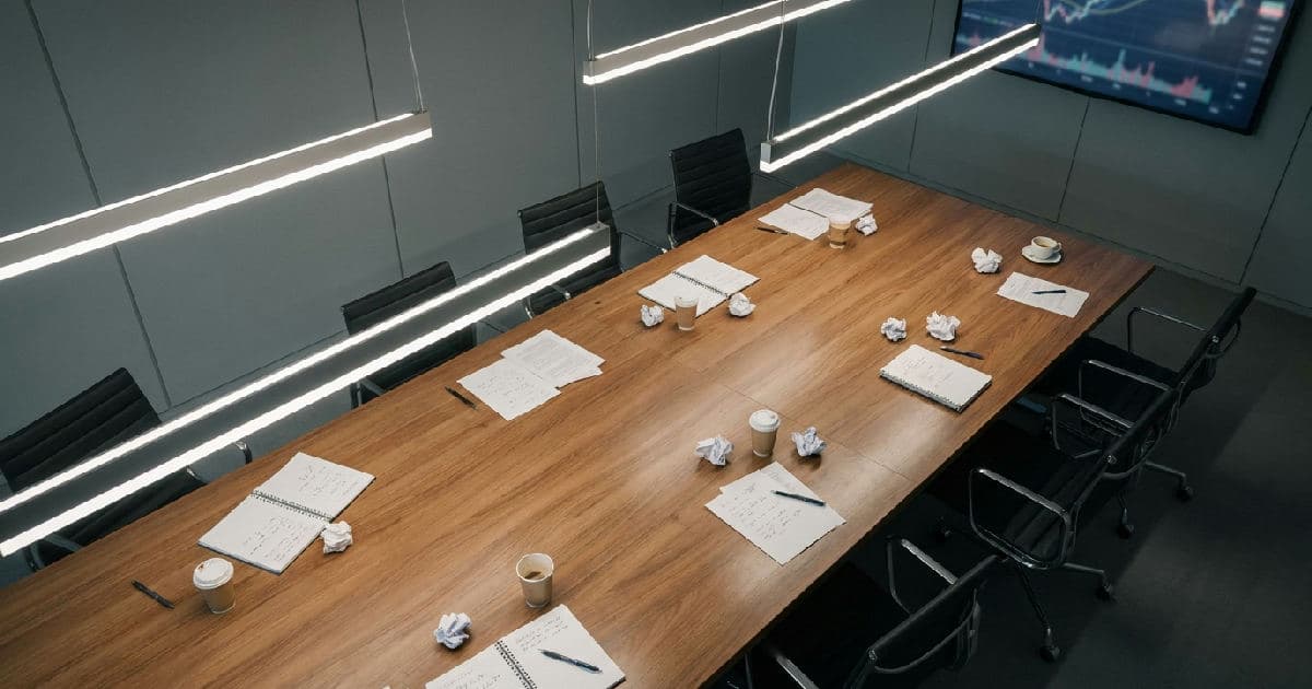 Empty boardroom table with papers, neutral lighting, suggesting corporate governance and shareholder tensions.