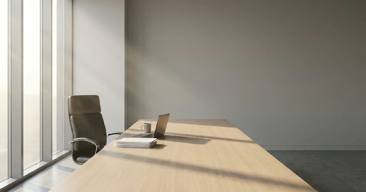 Empty boardroom with executive chair, wooden table, and morning light filtering through windows.