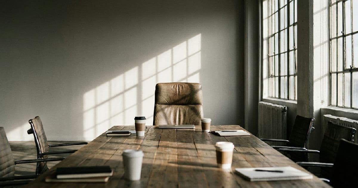 Empty boardroom with vacant chair at conference table, natural light, professional office setting.