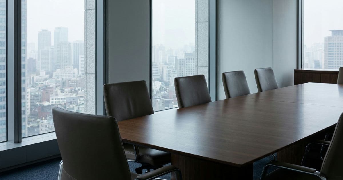 Empty boardroom with conference table and city views, suggesting institutional restructuring and change.