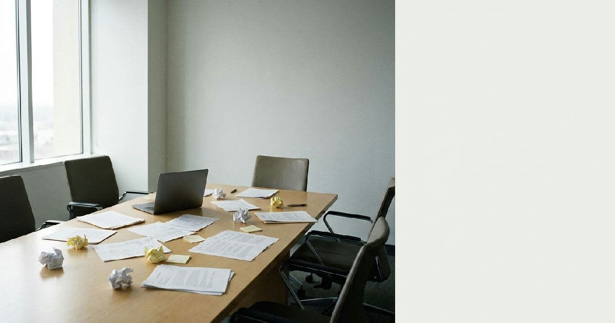 Empty boardroom table with papers and closed laptop, natural side lighting, professional office environment.