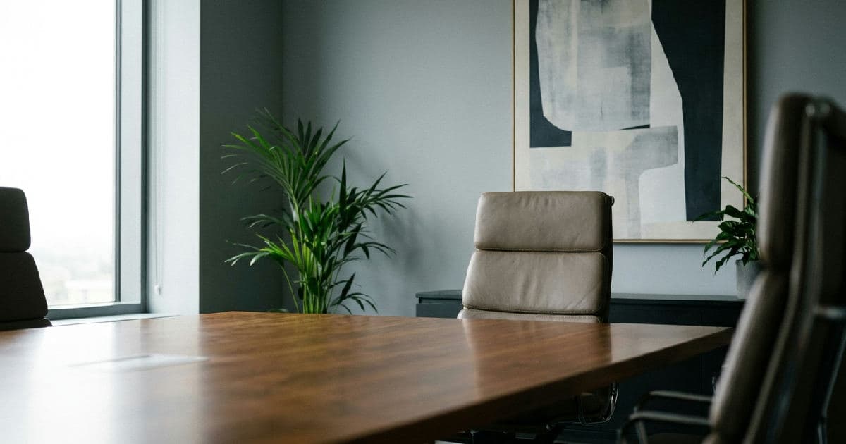 Empty boardroom with executive chair and table, natural lighting, professional office setting.