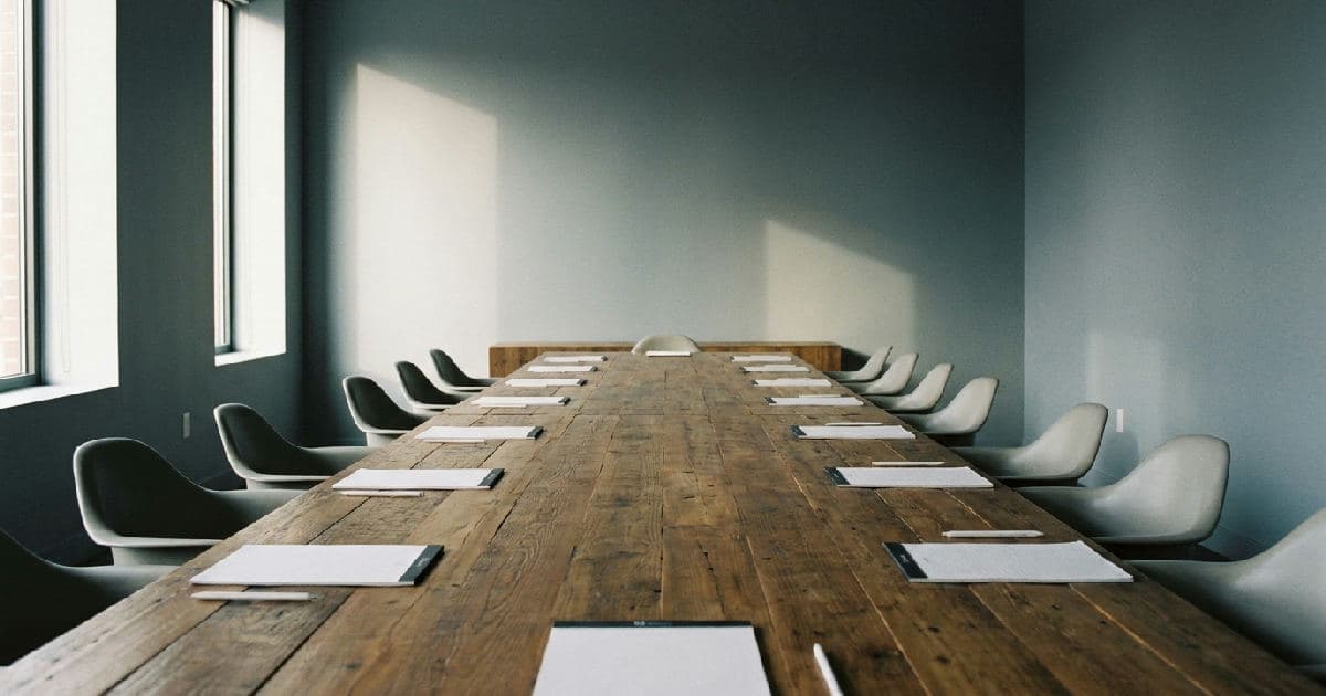 Empty modern boardroom with long table, papers, and natural side lighting.