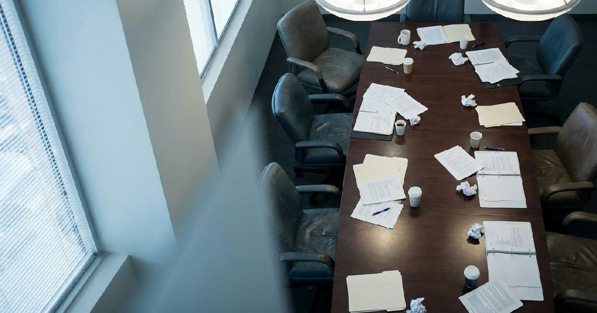 Empty boardroom table with scattered documents and chairs, professional office setting, overhead perspective.