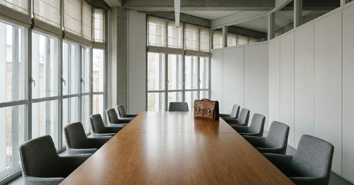 Empty boardroom table with chairs in neutral-toned professional office space.