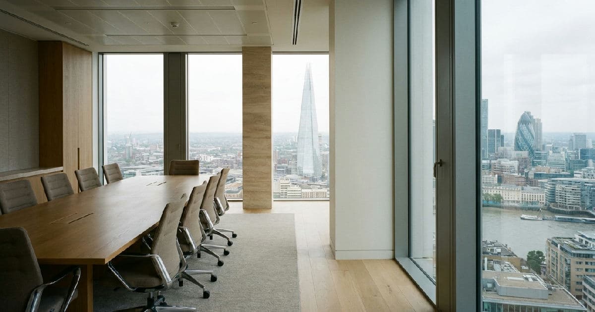 Empty modern boardroom with conference table overlooking London skyline through large windows.