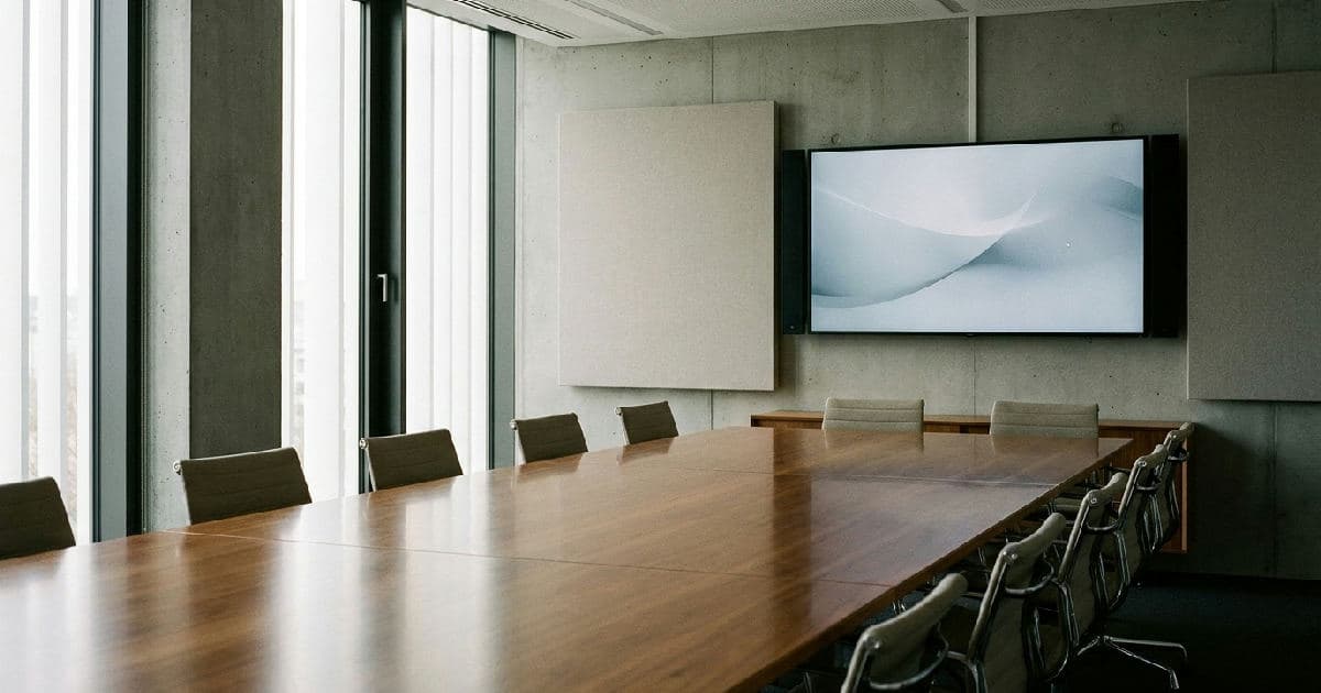 Empty modern boardroom with polished table, natural lighting, and minimalist furnishings.