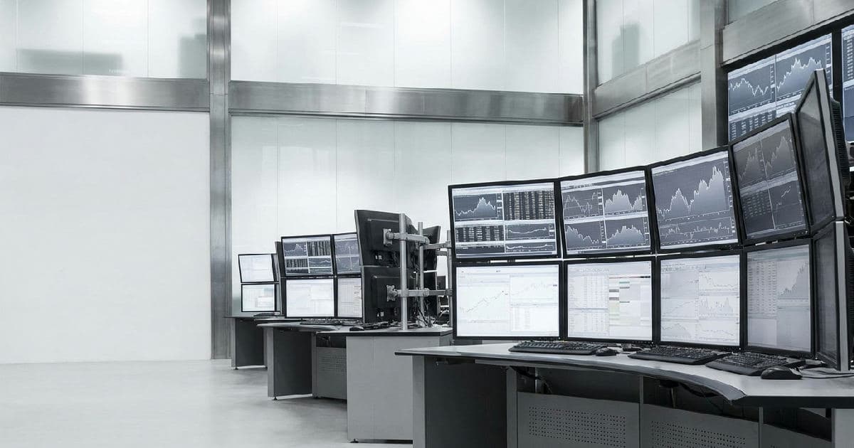 Trading floor screens displaying market data and financial charts in muted tones.