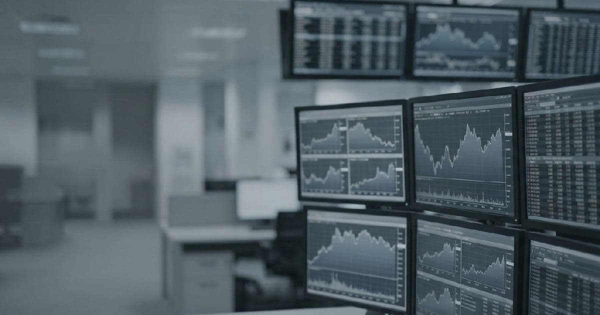 Multiple computer monitors displaying financial market data and charts in a trading environment.