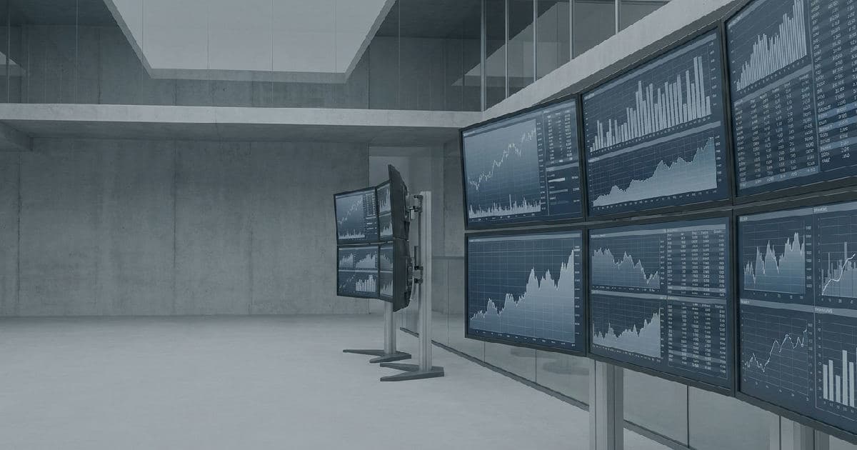 Trading floor monitors displaying financial data and market charts in desaturated tones.