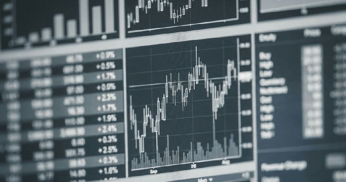 Multiple screens displaying abstract financial charts and market data in muted tones.