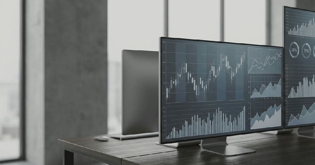 Multiple computer monitors displaying financial charts and market data in desaturated tones.
