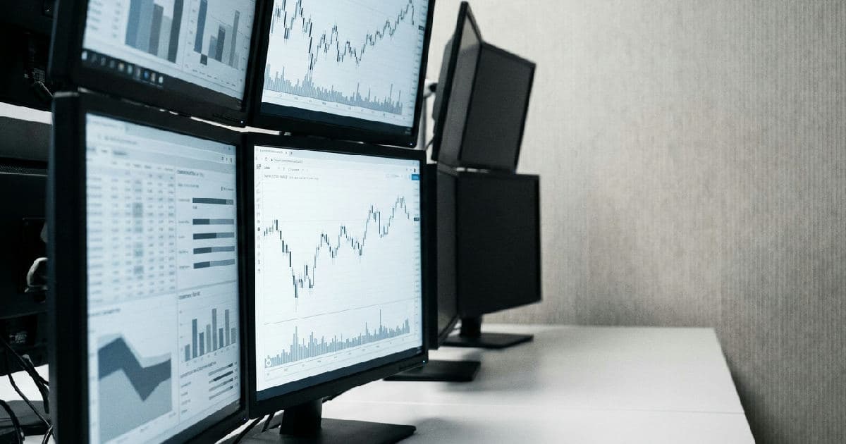Computer screens showing financial data visualisations and market charts in muted tones.