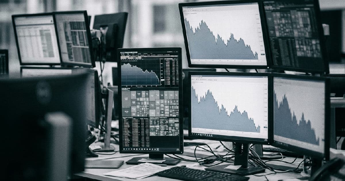 Multiple monitors showing downward trending market data visualisations on a trading desk.