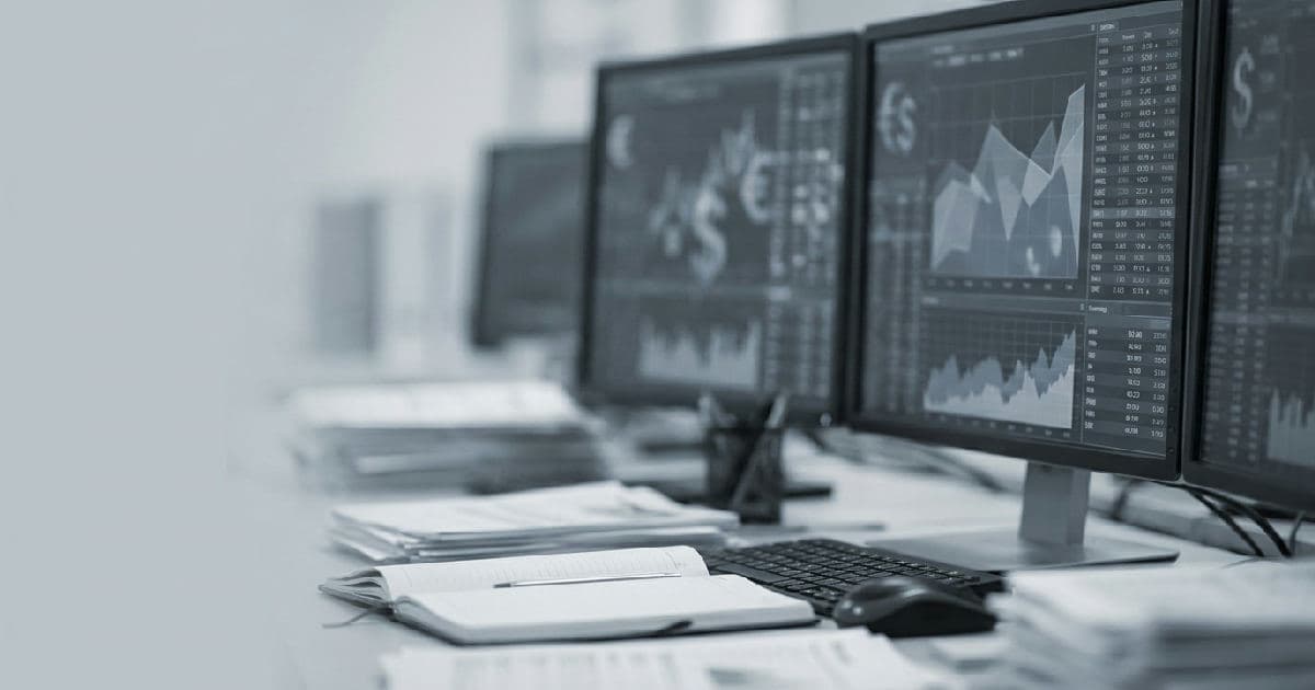 Multiple computer monitors displaying financial market data and charts on a trading desk.