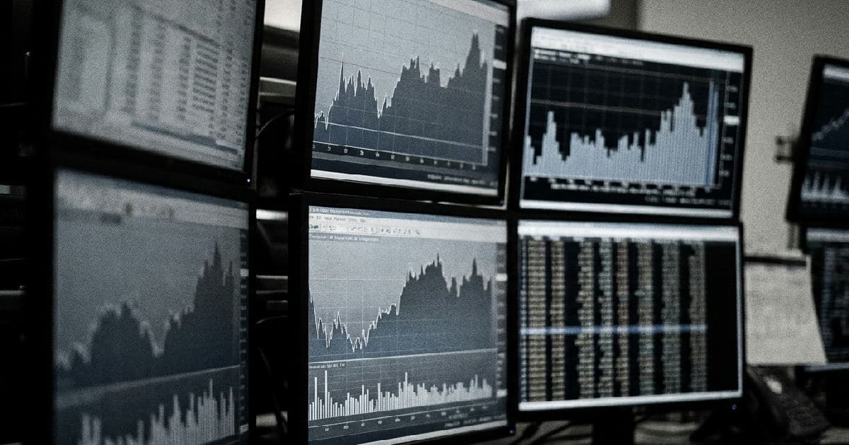 Multiple monitors displaying financial data visualisations and trend charts in desaturated tones.