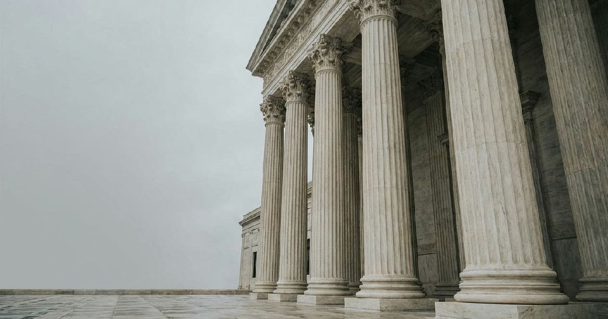 Classical marble columns of a government building facade under overcast sky.