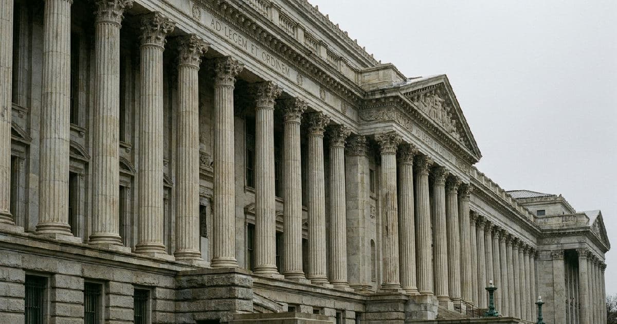 Classical marble columns of government building beneath overcast sky, architectural symbol of institutional oversight.