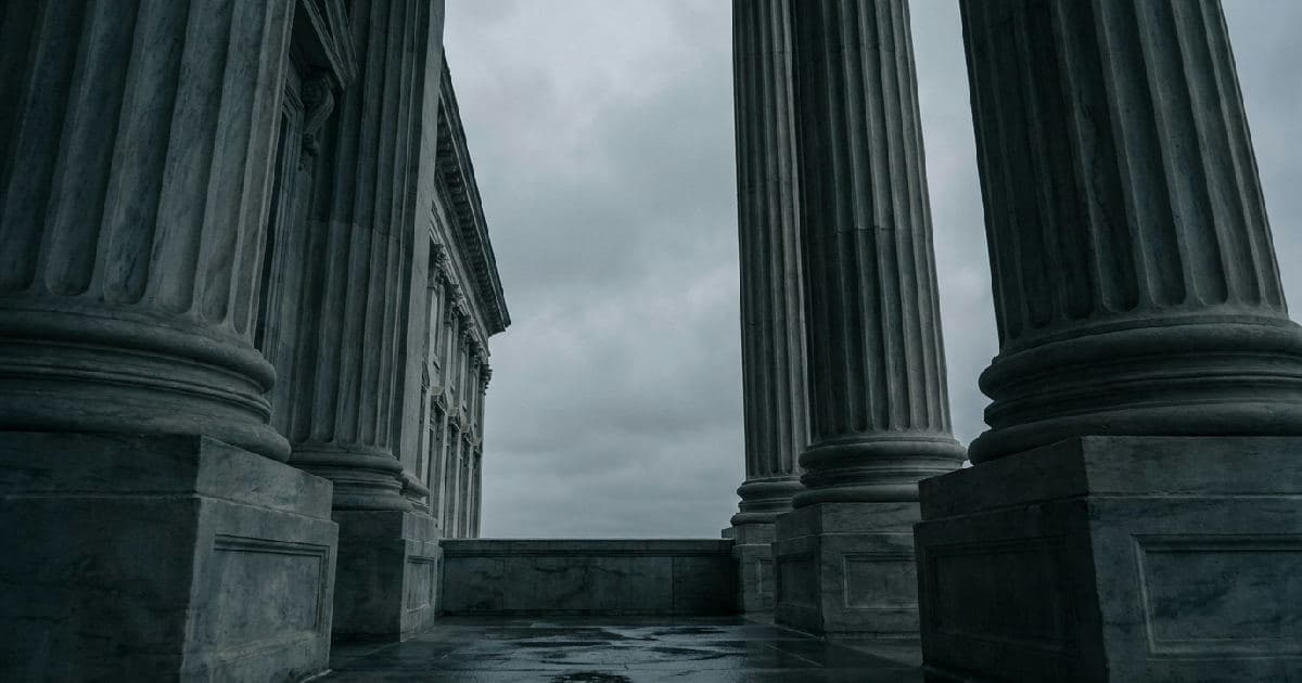 Classical marble columns of a government building beneath an overcast sky, photographed from below.
