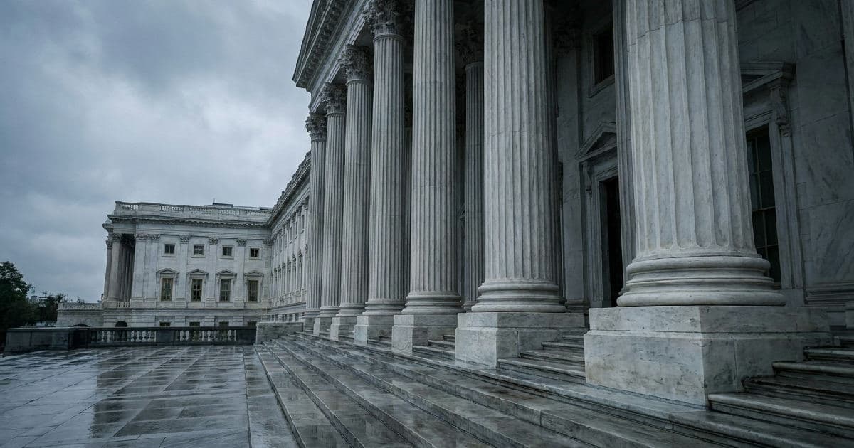Classical government building with marble columns beneath overcast sky, empty plaza setting.
