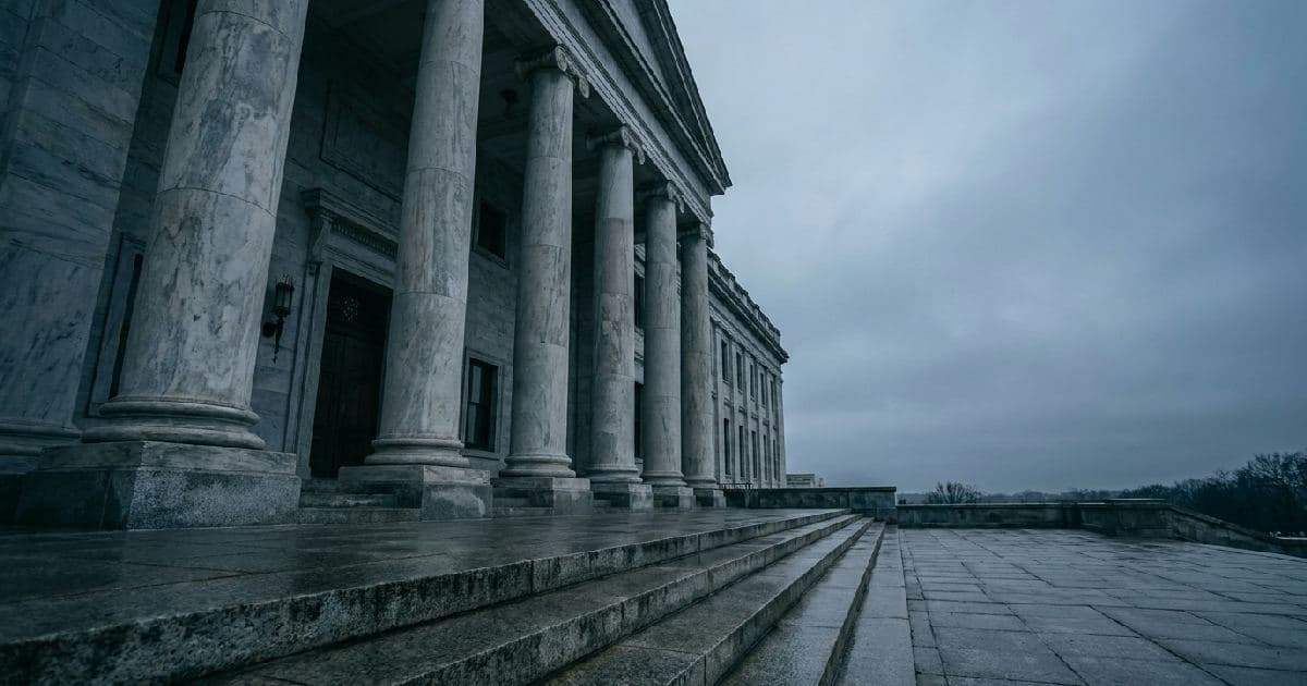 Classical marble columns of a government building beneath overcast sky, empty and austere.