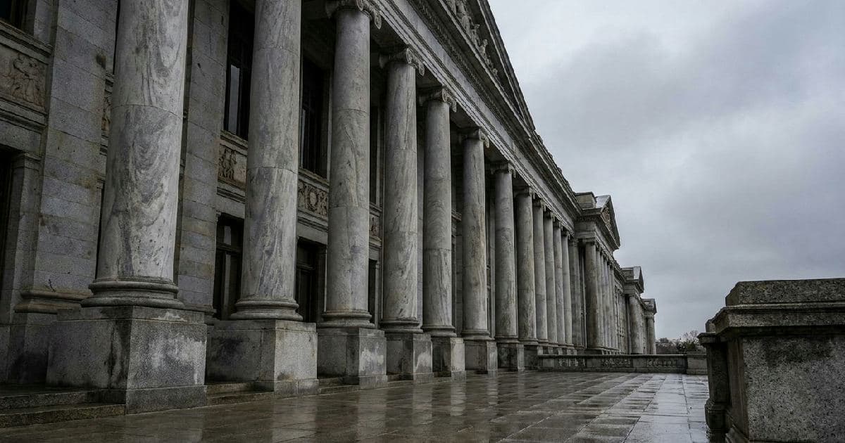 Marble columns of a government building facade beneath an overcast sky, emphasizing institutional authority.