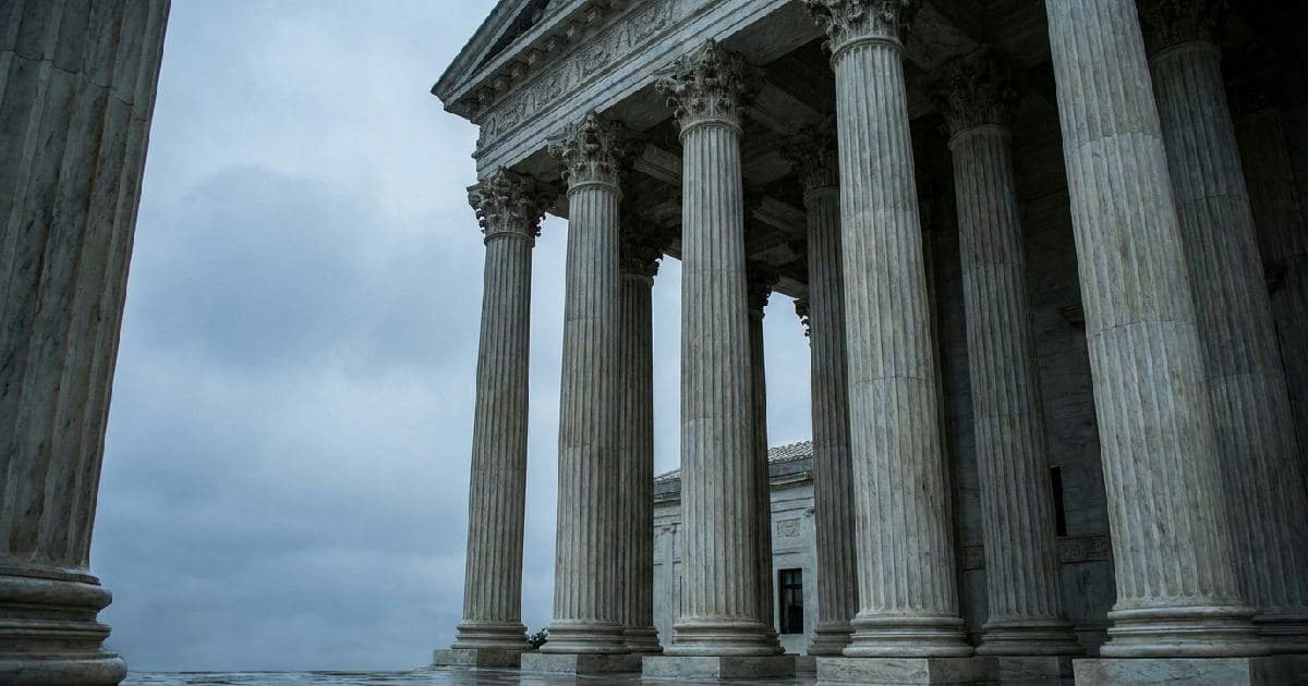 Classical marble columns of a government building beneath an overcast sky, emphasizing institutional weight and formality.