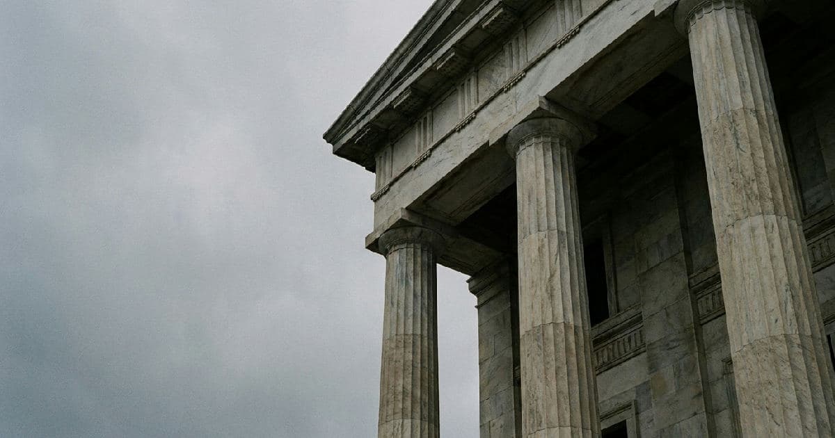 Classical marble columns of a government building under overcast sky, architectural detail emphasizing institutional authority.