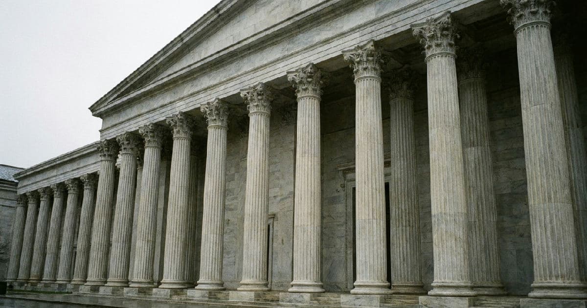 Classical marble columns of a government building under overcast sky, symmetrical architectural composition.
