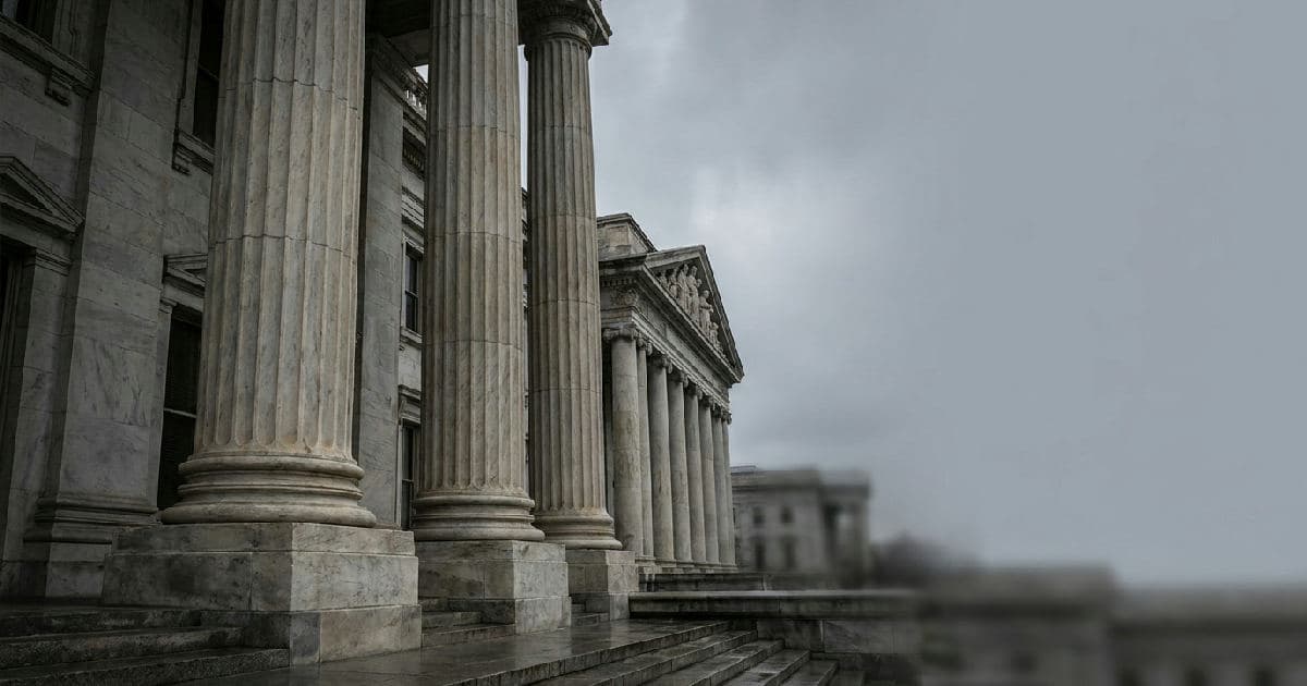 Classical marble columns of a government building under overcast sky, architectural detail suggesting regulatory authority.