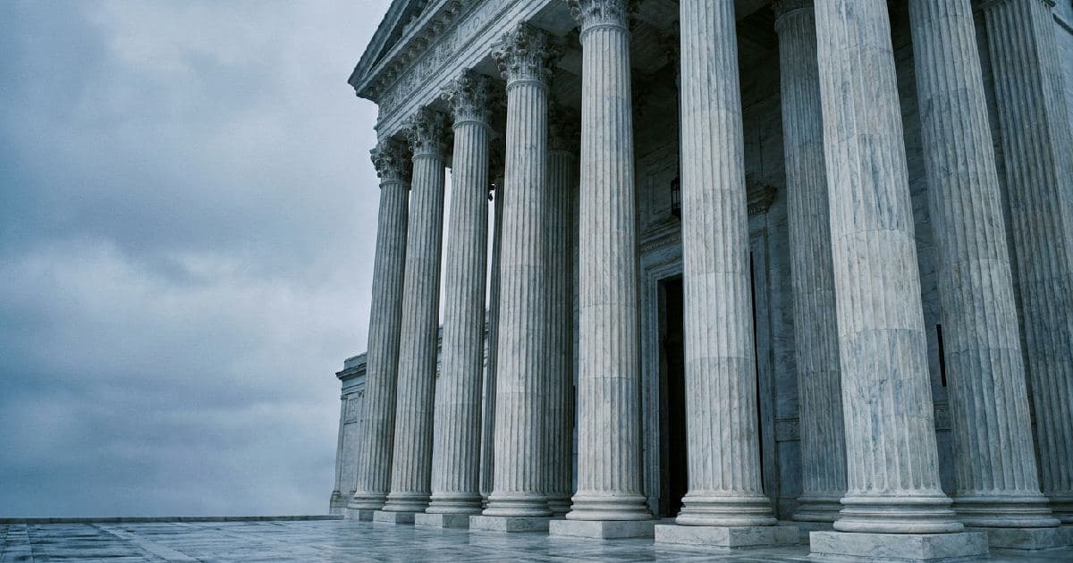 Classical marble columns of a government building exterior under overcast sky, empty courtyard.
