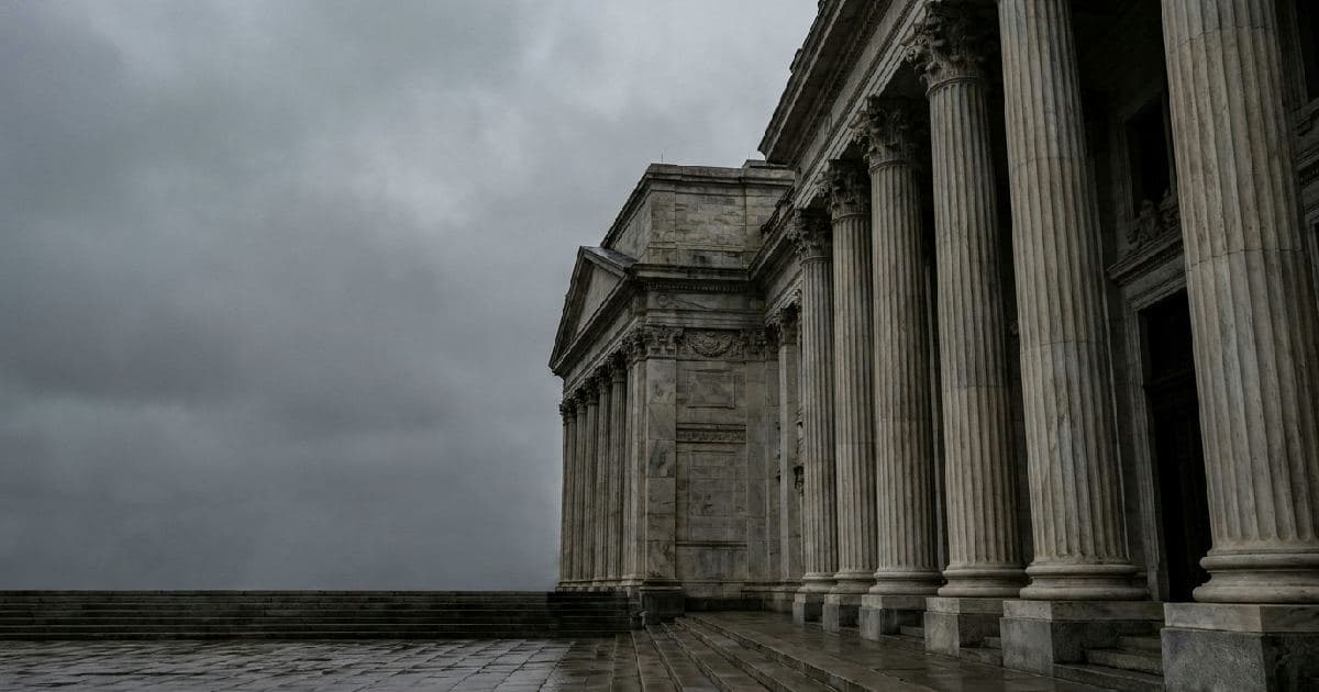 Classical marble columns of a government building under overcast sky, photographed from below.