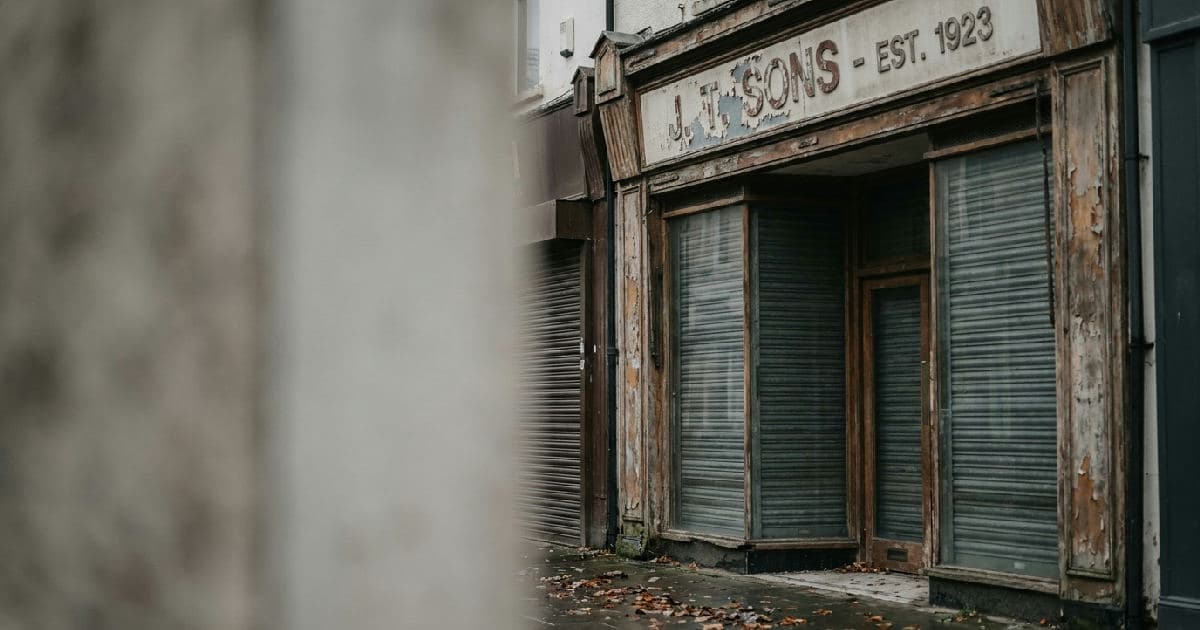 Empty high street storefront with closed shutters and weathered exterior signage.